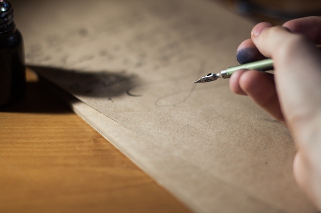 Človek, ktorý píše atramentovým perom na hnedý papier.jpg